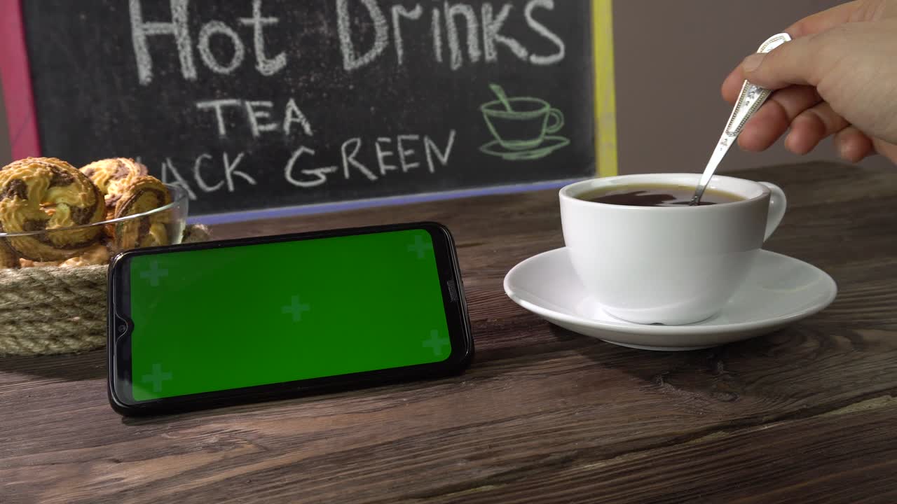 bebida caliente, galletas y teléfono inteligente en la mesa en el café. teléfono inteligente pantalla verde.