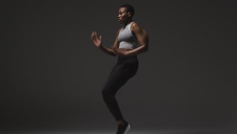 studio shot of woman wearing gym fitness clothing exercising running on the spot 3