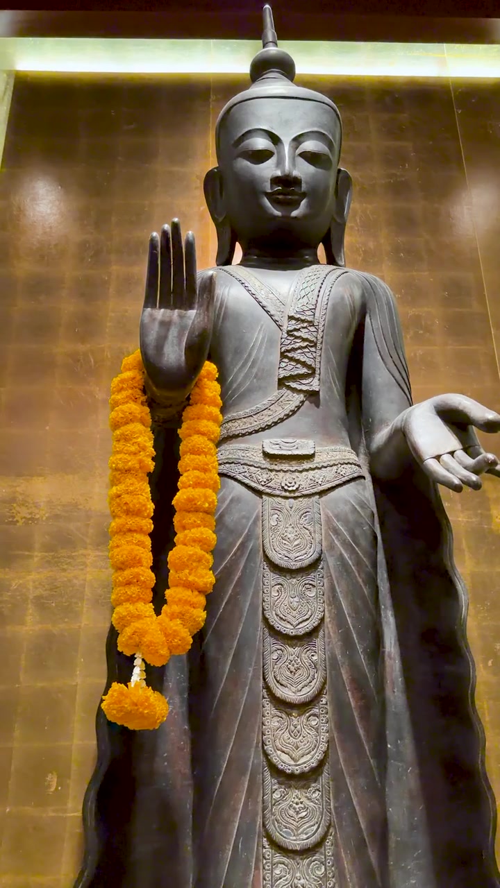 Una statua di Buddha in bronzo si erge su uno sfondo dorato con un lento zoom indietro