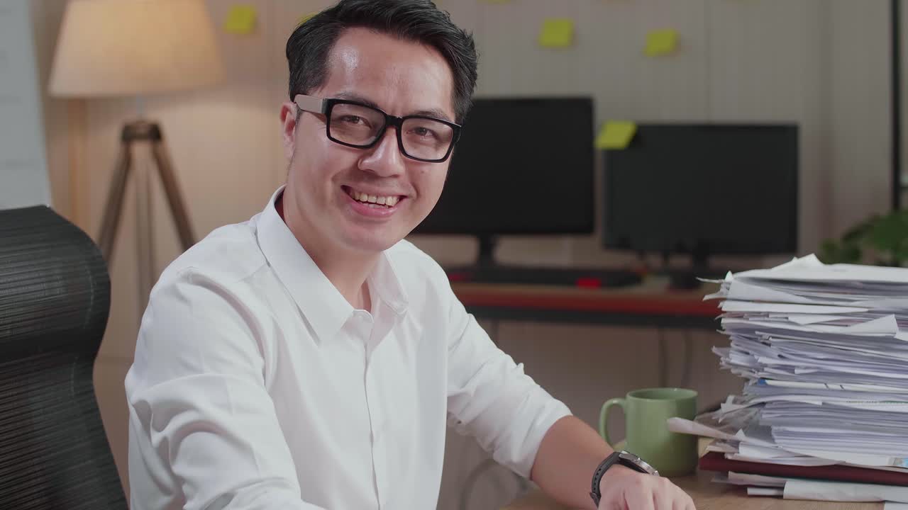Close Up Of Asian Man Smiling To Camera While Working With Documents At The Office