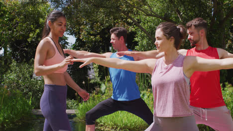 diverse group practicing yoga pose in sunny park with asian female instructor helping