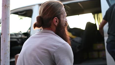 back view of the man looking the white car in front of him and another man pick up a sack from the car