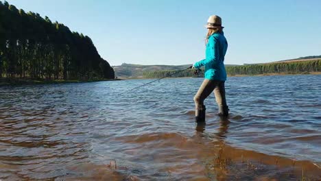 a girl fishing while standing in a beautiful lake next to a forest on a sunny day