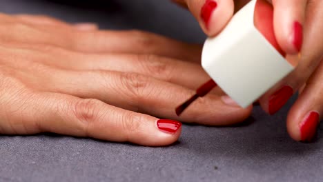 mujer pintando uñas con esmalte de uñas rojo vista lateral