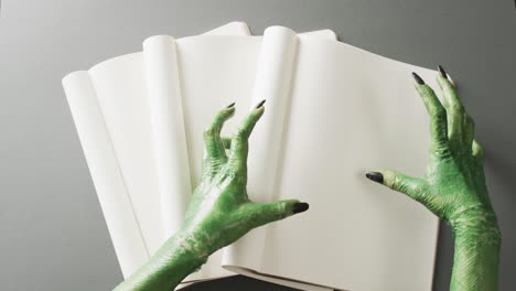 Video-of-halloween-green-monster-hands-and-notebook-with-copy-space-on-grey-background