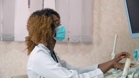 african american woman doctor in protective mask examines patient in ultrasound device monitor. concept of medicine, health care and people