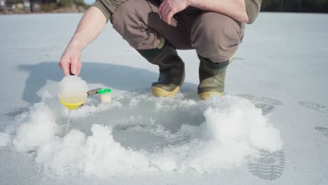 fisherman removing ice on fishing hole with plastic scooper