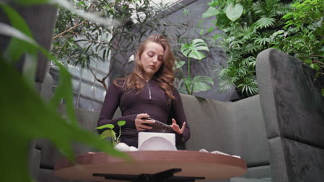 lady in black top and trousers stands in modern booth while taking overhead photo of waffles topped with strawberries and creamy sauce alongside latte on round wooden table with black stand