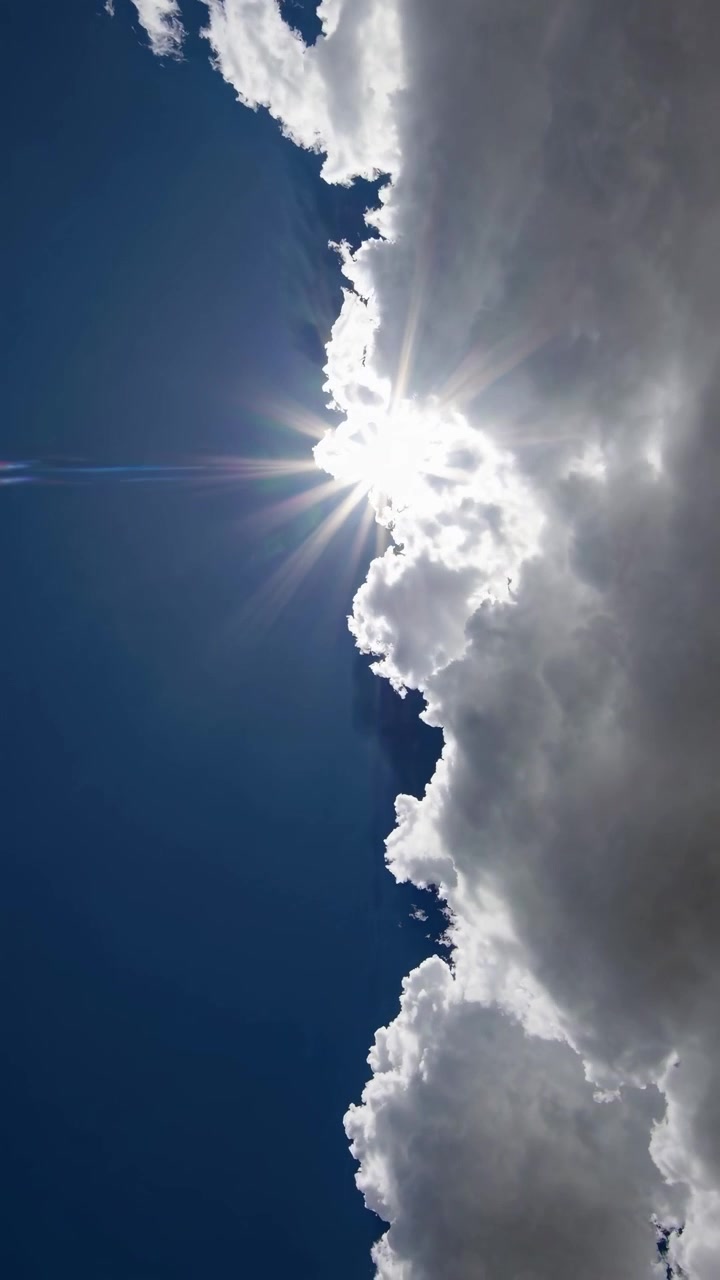 Bright Sun Shining Behind Fluffy White Clouds in Blue Sky