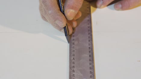 carpenter's hands measures the board with a ruler.