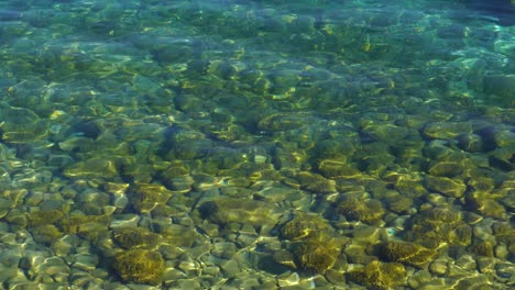 Fondo-Colorido-Del-Lago-Con-Guijarros-Que-Reflejan-Los-Rayos-Del-Sol-En-El-Agua-Transparente-Turquesa