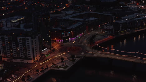 Aerial-view-of-cars-driving-through-roundabout-at-river-waterfront.-Low-traffic-in-night-city.-Limerick,-Ireland