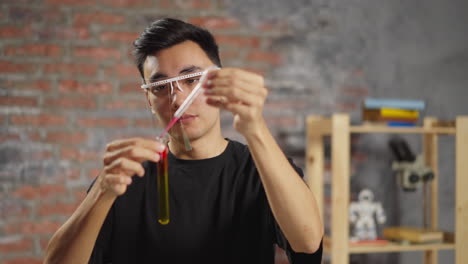un químico asiático añade reactivo en un tubo con líquido amarillo en el laboratorio.