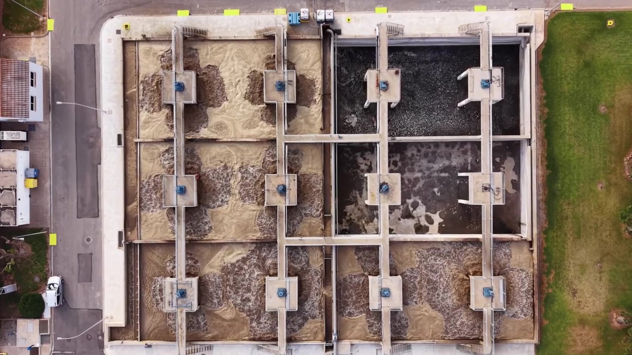 Vista dall'alto dei serbatoi bioreattori di un impianto di trattamento delle acque reflue urbane con fanghi attivi, che mostra i bacini di aerazione con acqua marrone e scura turbolenta