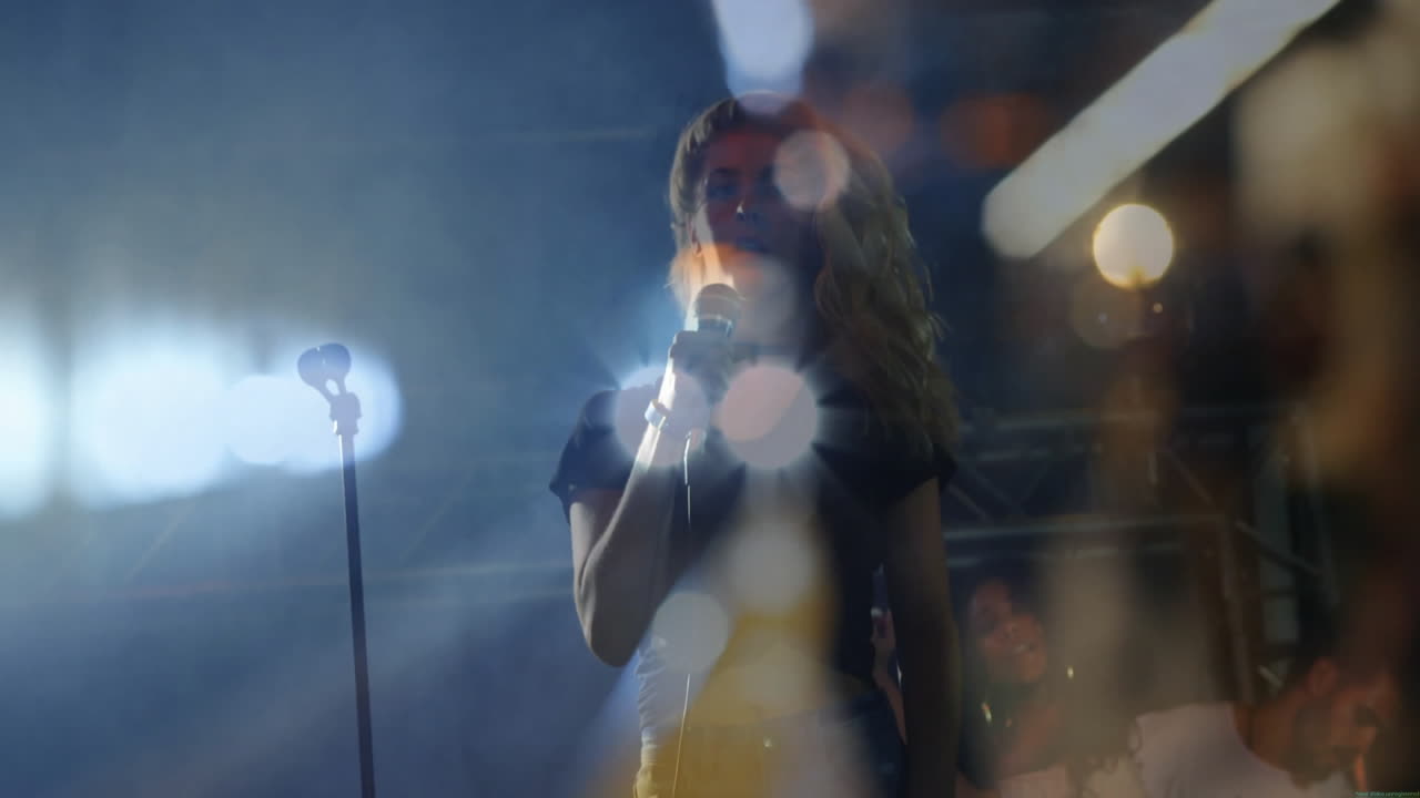 Female singer performing on hazy music stage with spotlights, gripping mic, showing waveforms