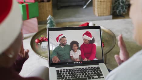 Diverse-senior-female-friends-using-laptop-for-christmas-video-call-with-happy-family-on-screen