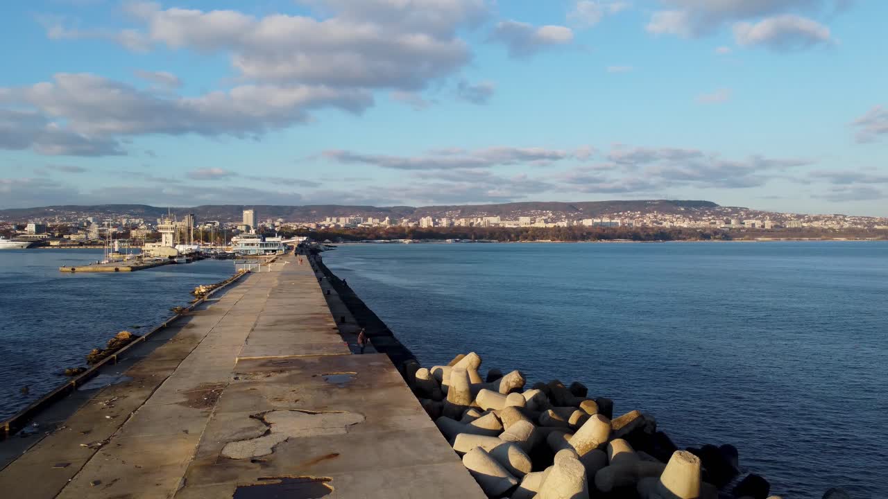 Panoramica da destra a sinistra di un molo vuoto al Porto di Varna durante il tramonto, con acqua blu ed edifici sullo sfondo.