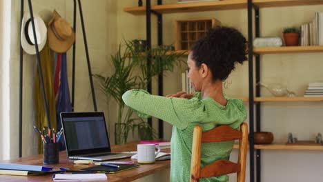 Mixed-race-woman-stretching-her-arms-while-working-from-home