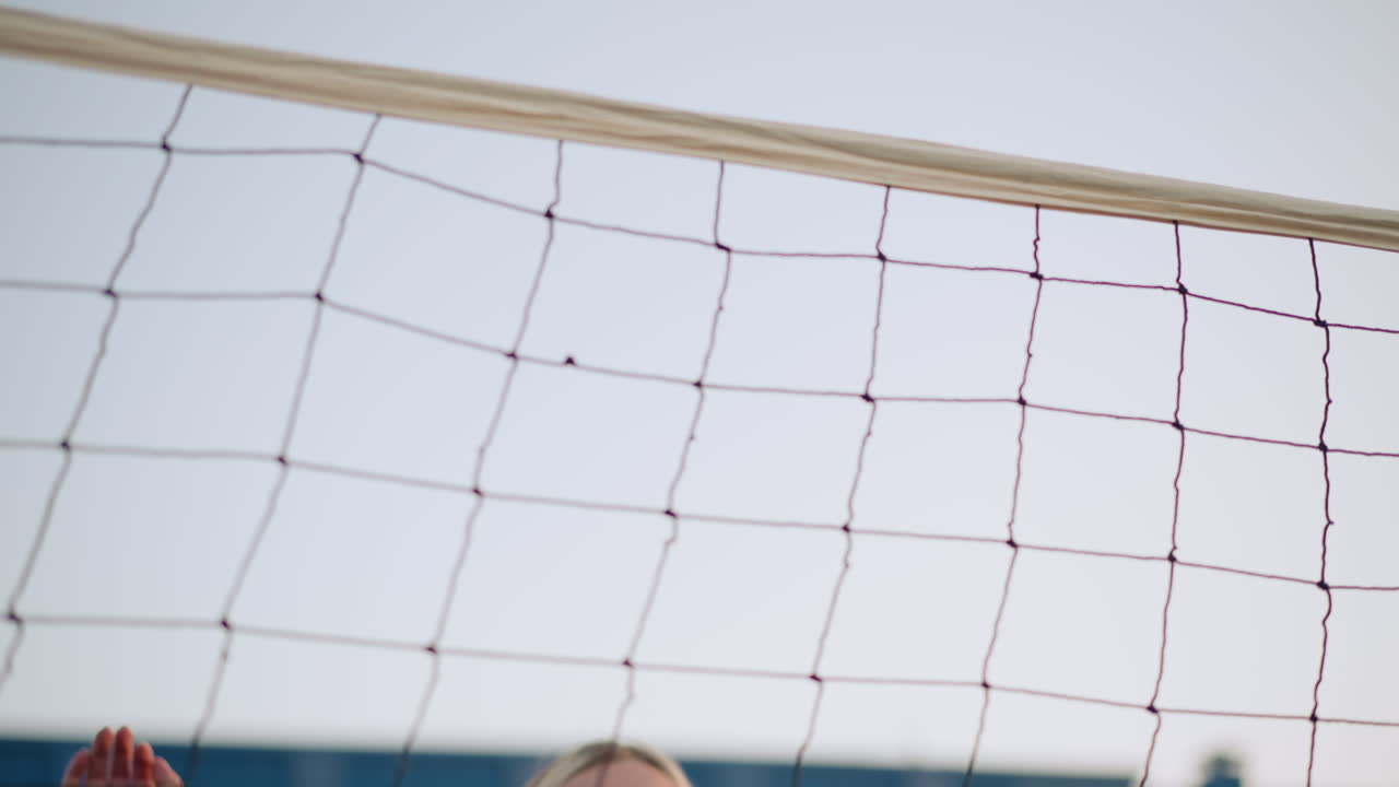 볼을 치기 위해 점프하고 준비하는 젊은 여성 선수의 클로즈업, 그녀의 표현과 결단력에 초점을 맞추고, 배경에는 볼 망과 건물이 있습니다.