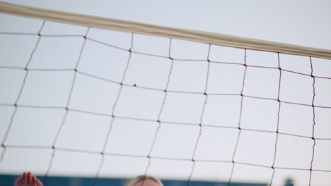 primer plano de una joven atleta que salta y se prepara para golpear el voleibol, con enfoque en su expresión y determinación, el fondo presenta una red de voleibol y edificios