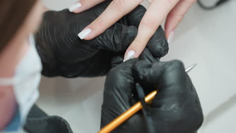 closeup of nail technician in black gloves carefully applying acrylic on client fingernail using small brush, demonstrating precision and focus in salon manicure process under bright lighting