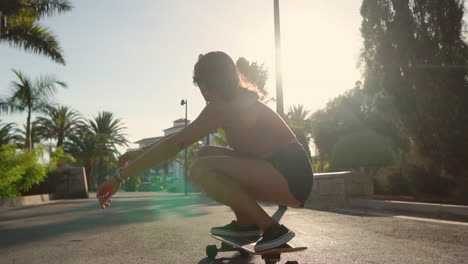 in slow motion, a young woman rides a longboard by palm trees in summer, wearing shorts and sneakers