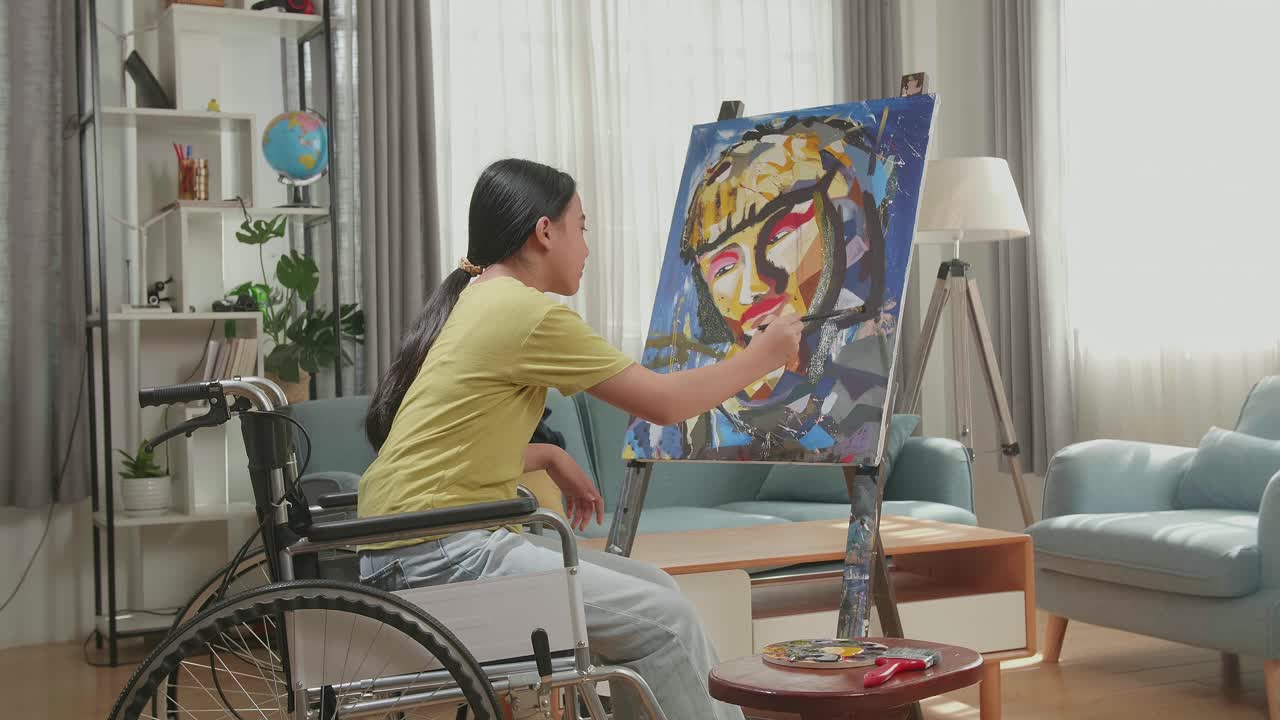 Side View Of An Asian Artist Girl In Wheelchair Holding Paintbrush Mixed Colour Thinking And Painting A Girl On The Canvas