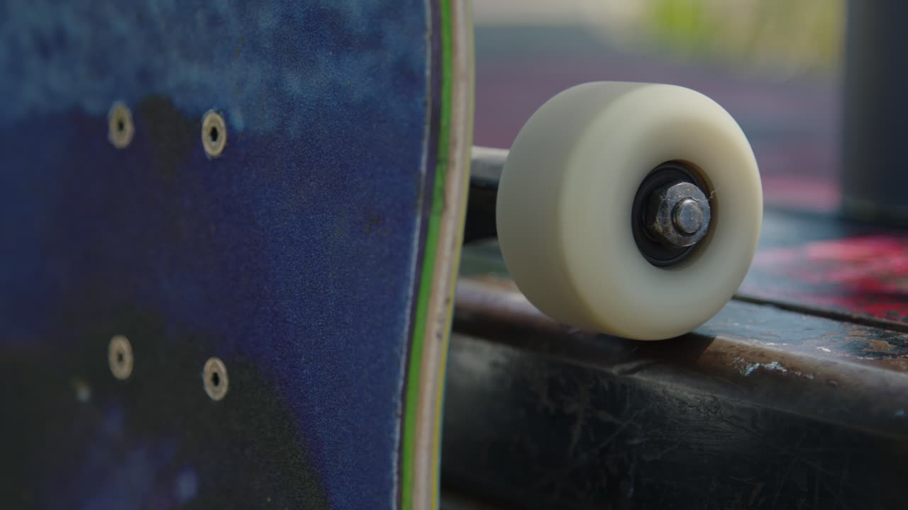 Close-up panning shot of a skateboard resting on a ledge at the skatepark, with the wheel spinning smoothly