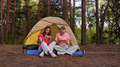 two friends camping and using their smartphones in a forest.