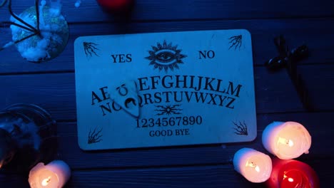 close up video of a wooden ouija board on a table surrounded by candles and a cross in a muffed - close up video of a wooden ouija board on a table. wax candles and a cross around. the planchette is slowly moving across the board, spelling out words and numbers. creative mystical content