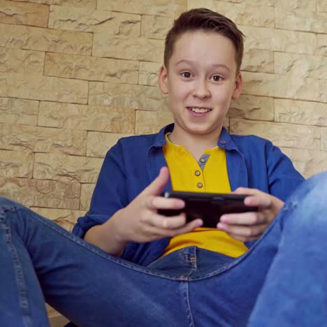 portrait of a boy with a smartphone at home. teenager is playing on his phone while sitting on stairs. social distancing and self isolation in quarantine.