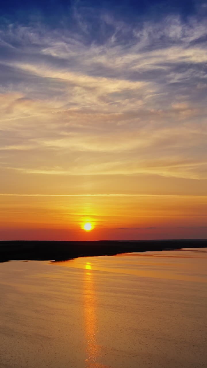 Amazing view on the river at sunset. Flight over the water under evening sky. Natural environment outdoors. Vertical video