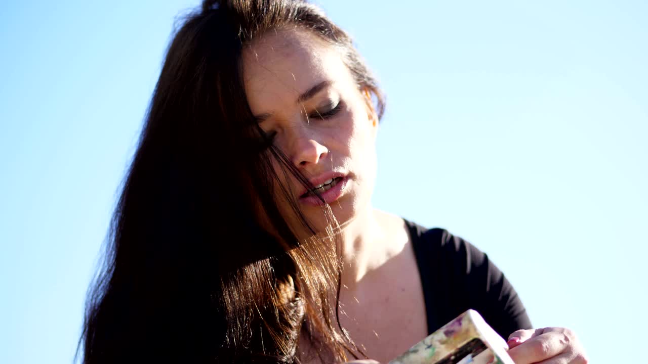 Una bella artista spreme un po' di vernice da un tubetto con un dispositivo speciale, un espediente. C'è un processo creativo. L'artista dipinge all'aperto, contro il cielo blu.