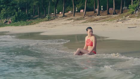 woman in swimsuit sits in ocean waves in evening slow motion