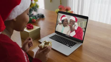 Mujer-Afroamericana-Con-Gorro-De-Papá-Noel-Usando-Una-Computadora-Portátil-Para-Una-Videollamada-Navideña,-Con-La-Familia-En-La-Pantalla