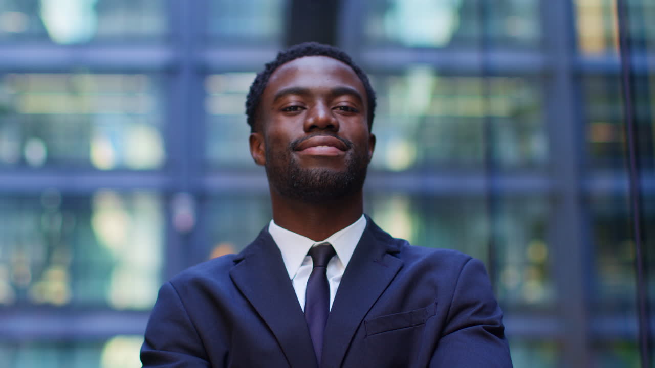 retrato de un joven empresario confiado y sonriente con traje y brazos plegados de pie fuera de las oficinas en el distrito financiero de la ciudad de londres, reino unido.