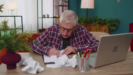 Abuelo-Trabajando-En-Una-Computadora-Portátil-Hombre-Escribiendo-En-Una-Hoja-De-Papel,-Enojándose,-Arrugándola,-Tirándola