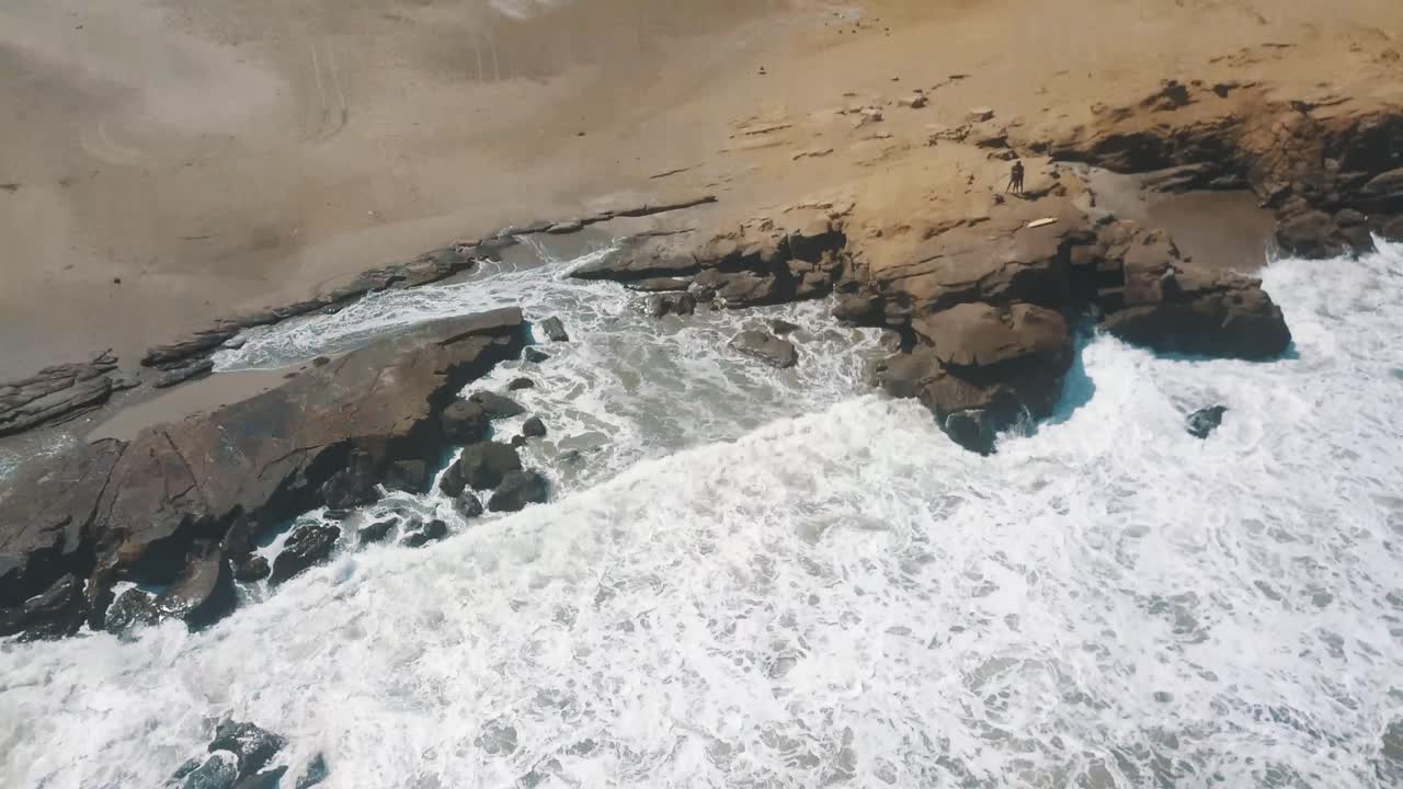 agua de mar espumosa salpicando contra la costa rocosa en la playa de lobitos, perú durante el día soleado de verano - toma aérea de drones