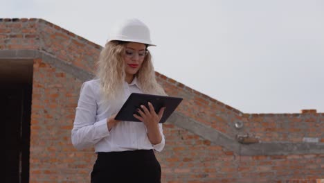 female architect in business attire stands in a newly built house with untreated walls and works on a tablet. modern technologies in the oldest professions