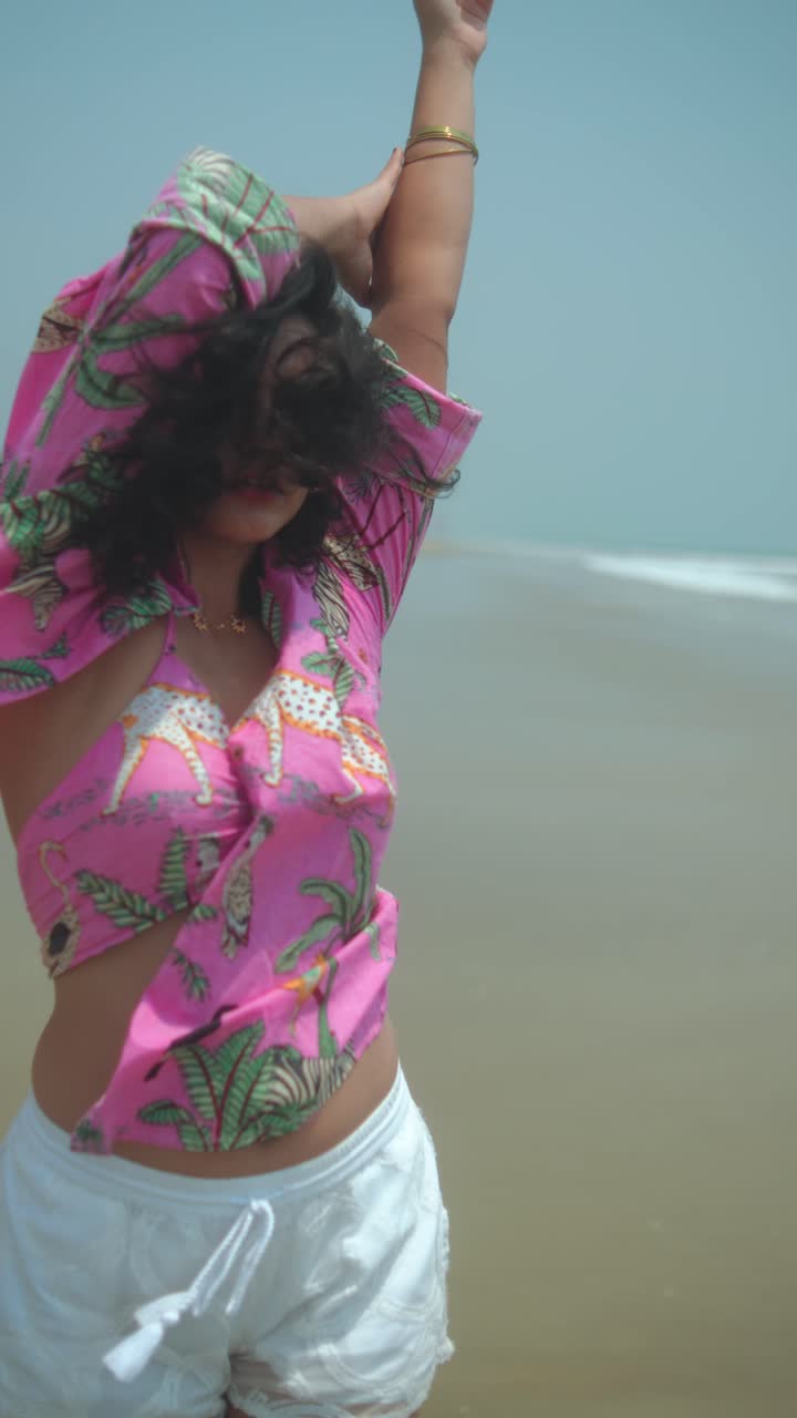 Confident woman posing on the beach in pink tropical shirt, relaxed summer mood