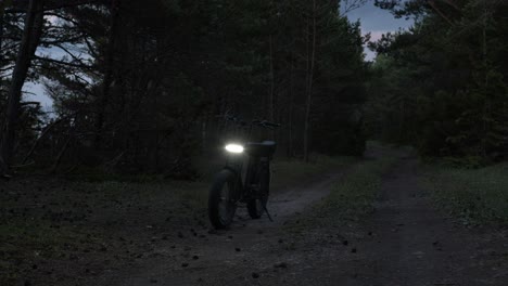 electric bicycle parked on country road during sunset with front light turned on, trees moving in wind