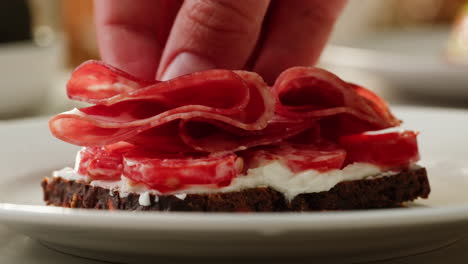 Hand Placing Ham on a Gourmet Sandwich