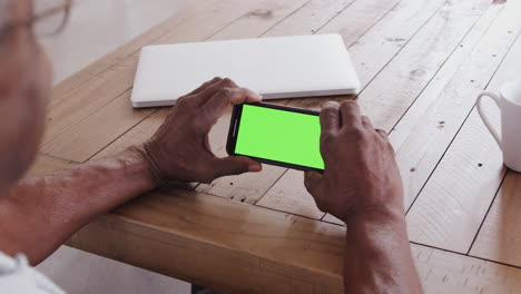 vista sobre el hombro de un hombre negro mayor en una mesa de madera usando un teléfono inteligente horizontalmente, de cerca