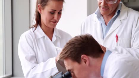 chemist looking at a microscope with colleagues behind him