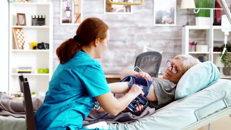 nurse measuring blood pressure of old sick lady laying in hospital bed