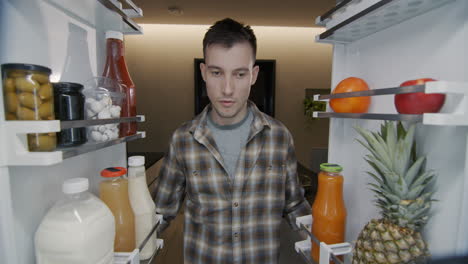 a man takes a red apple from the refrigerator. light snack and healthy eating concept