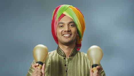 Close-up-view-of-cheerful-Indian-man-in-traditional-clothes-and-turban-playing-maracas-and-smiling-at-the-camera