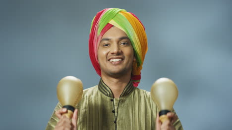 vista de cerca del alegre hombre indio con ropa tradicional y turbante tocando maracas y sonriendo a la cámara