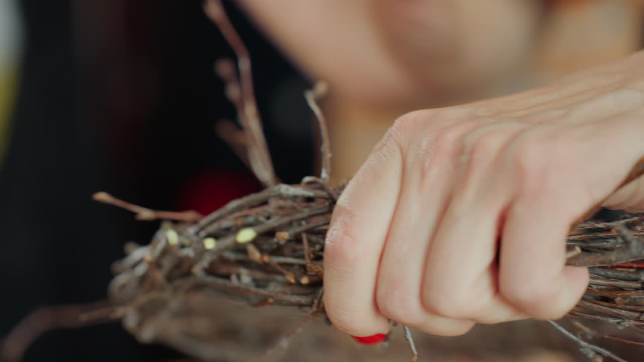 Female florist hands with red nails holding twig wreath close up, showing detailed process of arranging natural branches for rustic handmade decoration, highlighting artisanal craftsmanship