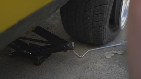 a man with a lifting jack lifts a yellow car with a flat tire